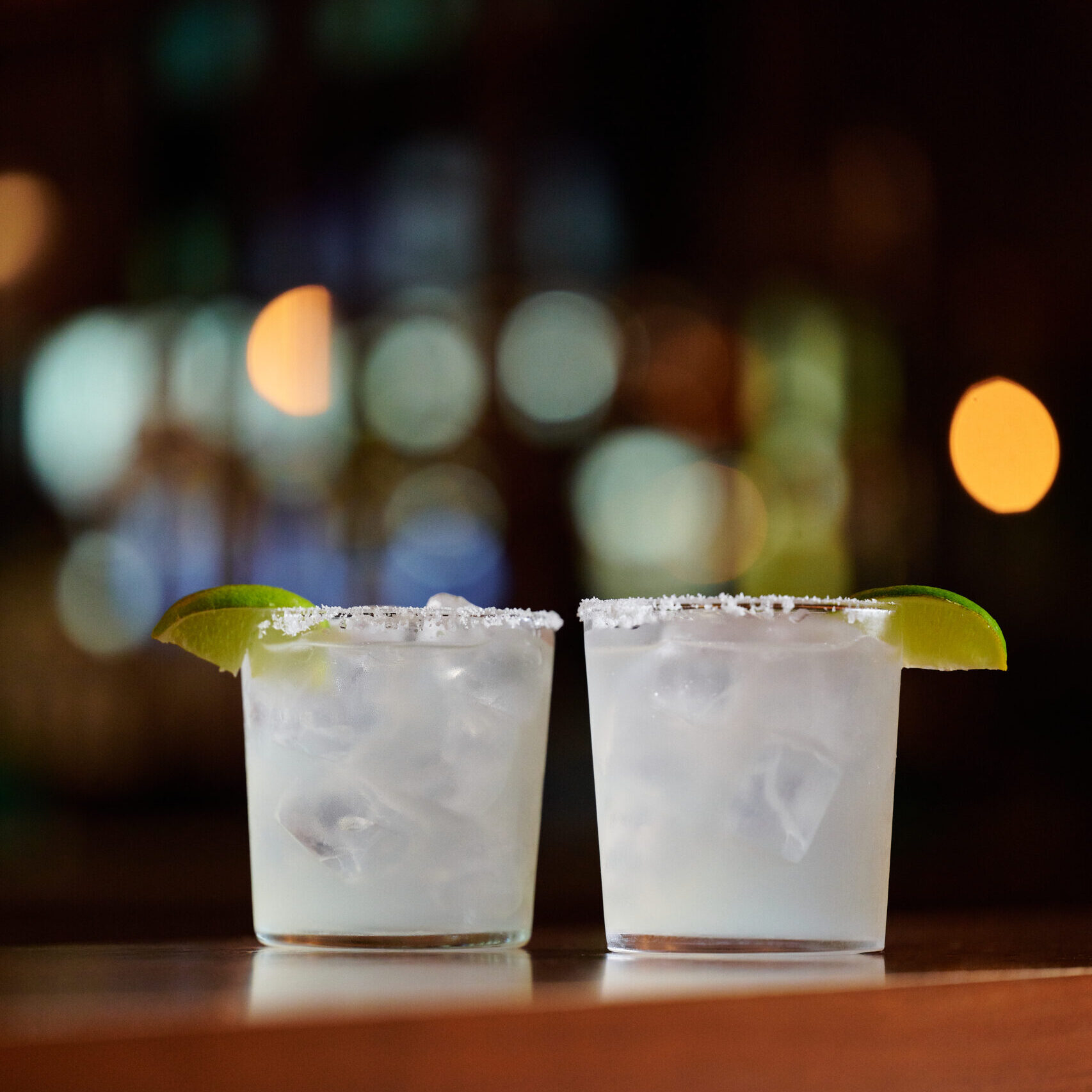 Two salt-rimmed margaritas garnished with lime wedges on a bar, highlighting Happy Hour at Pisco y Nazca.