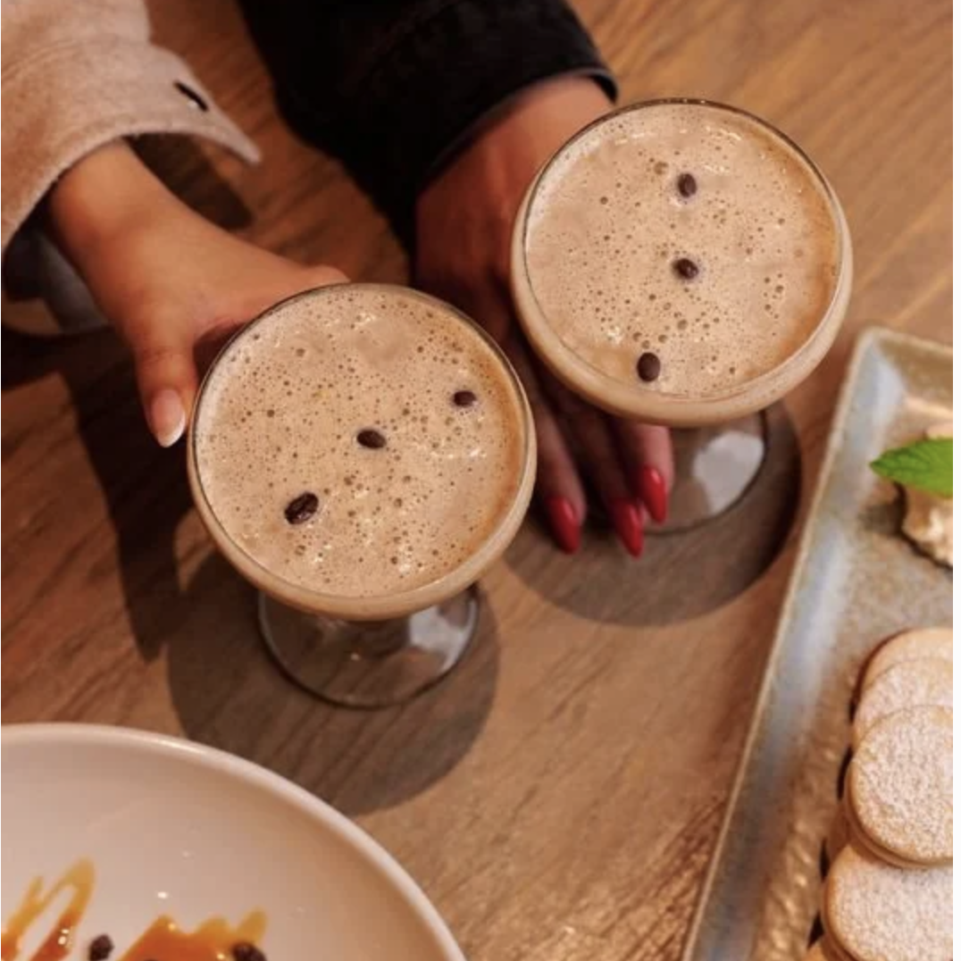 espresso martinis topped with coffee beans, surrounded by alfajores and a plated dessert on a wooden table.