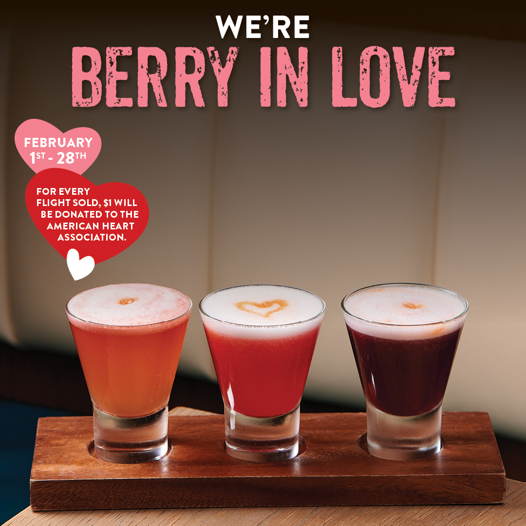 Valentine’s Day berry cocktail flight featuring three red and pink drinks with heart foam details on a wooden board, promoting Pisco y Nazca’s “We’re Berry in Love” special available February 1–28 with a donation to the American Heart Association.